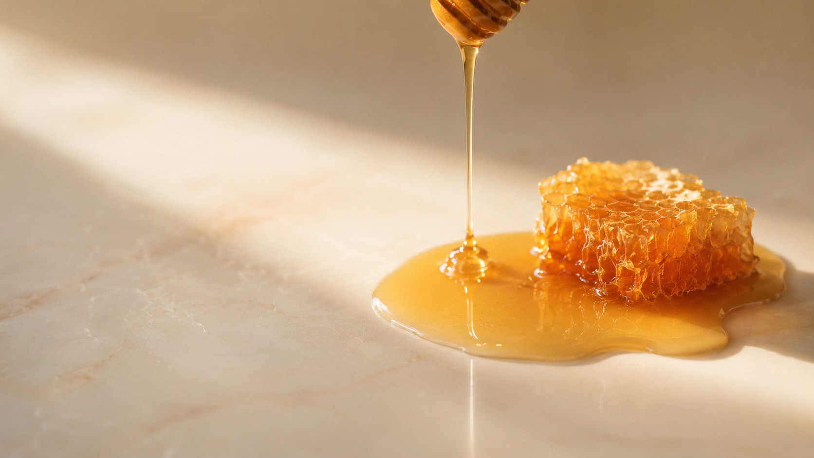 Favo di miele e una goccia dorata su superficie chiara, immagine calda ed elegante che richiama la parola mellito
