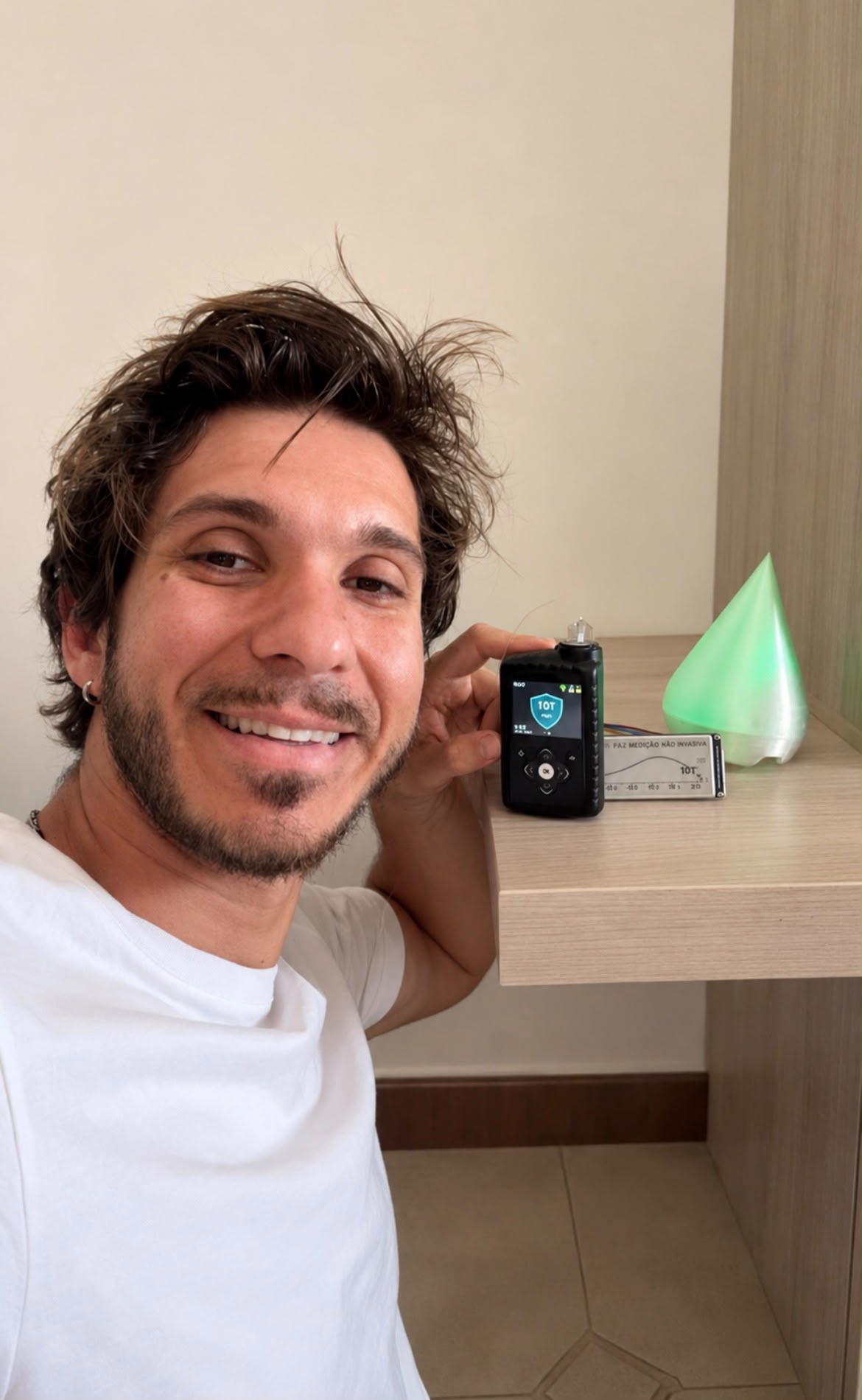 Fabio sorride accanto al suo microinfusore, alla lampada verde e all'accessorio che prevede la glicemia