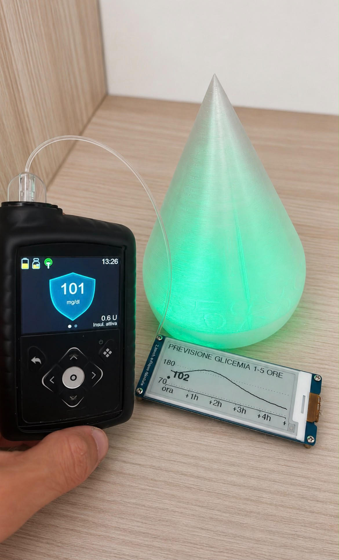 Un microinfusore che segna 101 mg/dl, una lampada a goccia accesa di verde e l'accessorio con schermo e-ink che mostra la previsione della glicemia da 1 a 5 ore